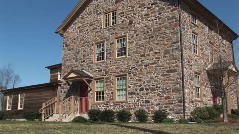The-Camera-Zooms-In-On-Threestory-Fieldstone-House-To-Focus-On-Ground-Level-Windows-And-Red-Front-Door
