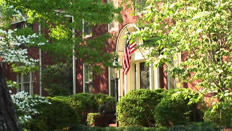 An-American-Flag-Seen-Through-The-Trees-Hangs-Proudly-Beside-A-Home'S-Doorway