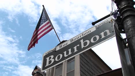 Eine-Amerikanische-Flagge-Weht-über-Einem-Straßenschild,-Das-Die-Berühmte-Bourbonstraße-Von-New-Orleans-Kennzeichnet-Identifying