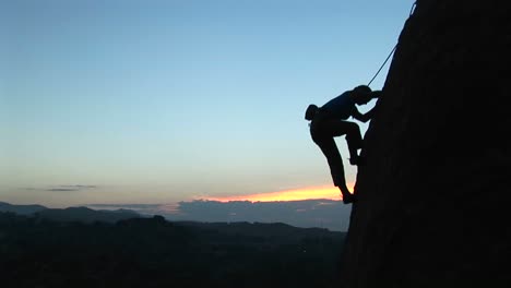 Longshot-Of-A-Rock-Climber-Scaling-A-Cliff-Silhouetted-Against-A-Goldenhoursky