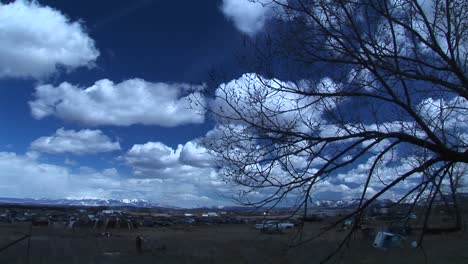 Wide-Shot-Of-Sky-In-Colorado-With-Car-Graveyard-And-Tree-Branch-In-The-Foreground-And-Rocky-Mountains-In-The-Background