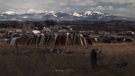 Mediumshot-Of-A-Car-Junkyard-In-Front-Of-The-Scenic-Rocky-Mountains
