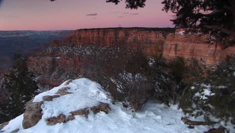 Wide-Shot-Of-Grand-Canyon-National-Park-With-Foreground-Of-Cliffs-Edge-And-Snowcovered-Rocks-Shrubs-And-Trees