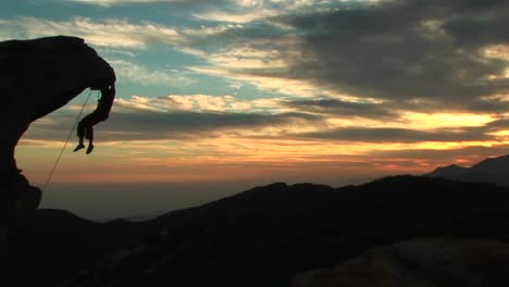 Panleft-Of-A-Silhouetted-Rockclimber-Hanging-From-An-Overhanging-Rock-Face-With-California-Sunset-Beyond