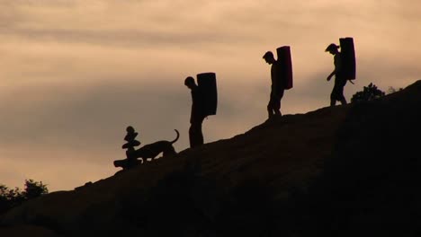 Panleft-Of-Three-Backpackers-And-A-Dog-Silhouetted-Against-An-Evening-Sky