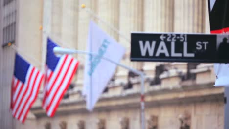 Pull-focus-shot-between-American-flags-and-a-sign-of-Wall-St-in-New-York-City