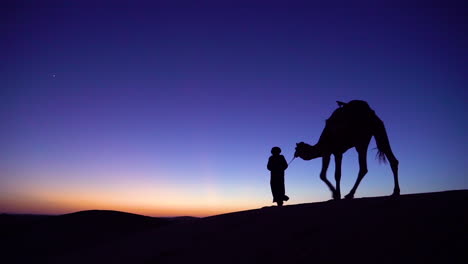 A-classic-travel-adventure-shot-of-a-man-leading-a-camel-across-a-dune-in-silhouette-1