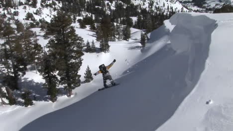 Following-shot-of-a-snowboarder-jump-off-a-slope-and-landing-in-deep-powder