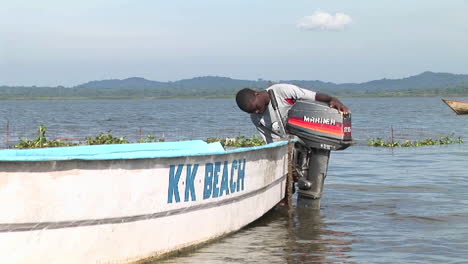 Zoom-Eines-Jungen-Mannes-Aus-Uganda,-Der-Einen-Außenbordmotor-An-Ein-Fischerboot-Anbringt