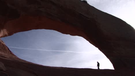 A-person-walks-beneath-a-giant-sandstone-arch-in-Arches-National-Park-Utah
