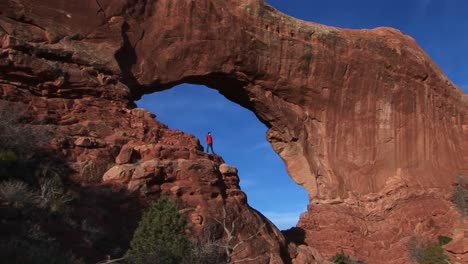 A-hiker-stands-on-a-ledge-at-Arches-National-Park-Utah